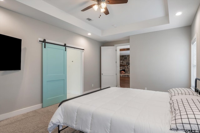 bedroom featuring a raised ceiling, a barn door, ceiling fan, and carpet flooring