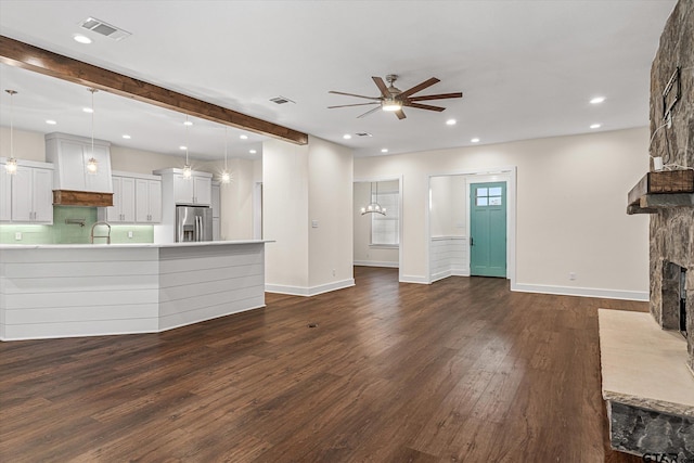 unfurnished living room featuring a stone fireplace, sink, ceiling fan, beamed ceiling, and dark hardwood / wood-style flooring