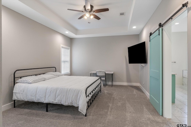 bedroom featuring a barn door, a tray ceiling, ensuite bath, and ceiling fan