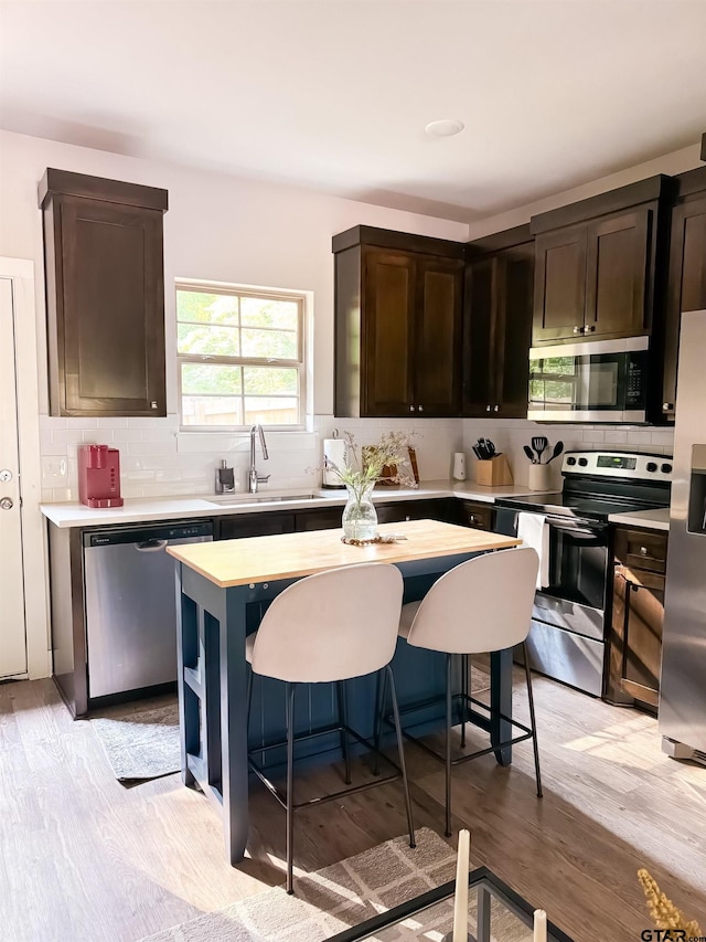 kitchen with light wood-type flooring, dark brown cabinetry, stainless steel appliances, sink, and a center island