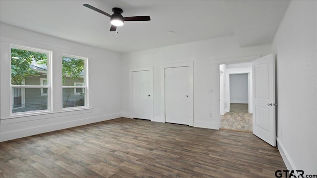 unfurnished bedroom featuring dark hardwood / wood-style flooring, two closets, and ceiling fan