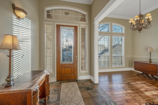 foyer featuring a chandelier, ornamental molding, stone tile flooring, and baseboards