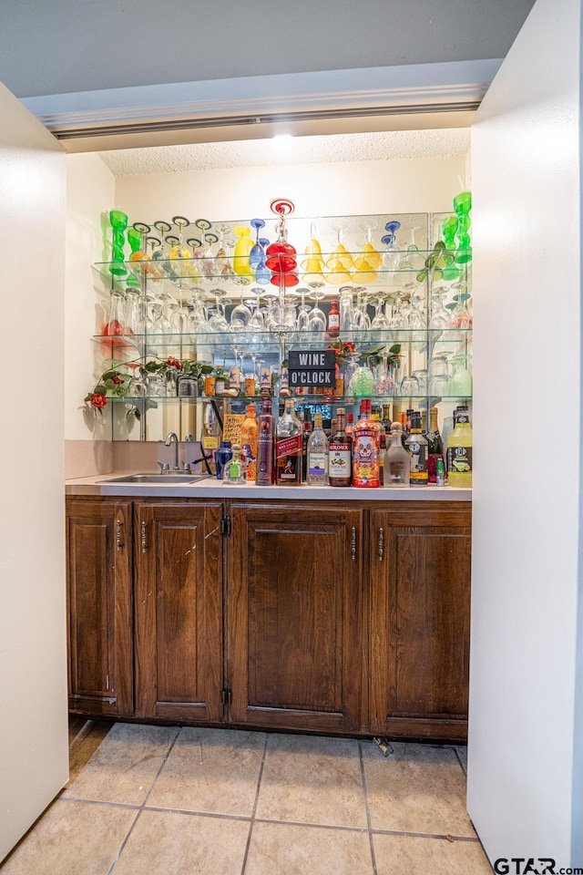 bar featuring light tile patterned floors, dark brown cabinetry, and sink