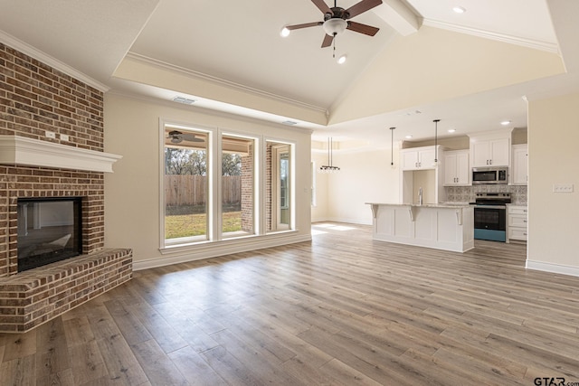 unfurnished living room featuring ornamental molding, ceiling fan, a brick fireplace, beam ceiling, and light hardwood / wood-style flooring