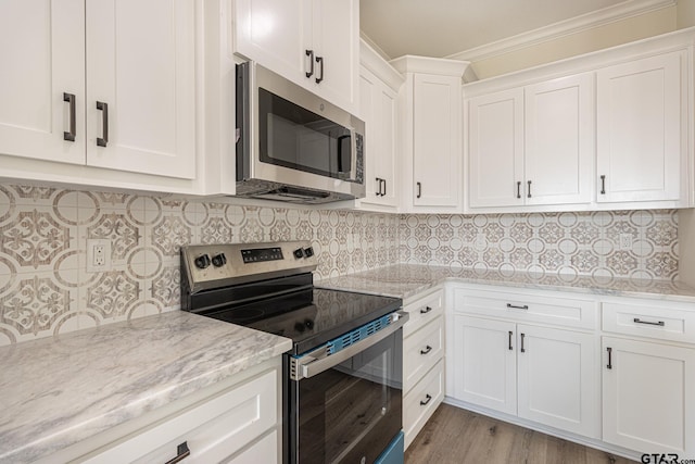 kitchen with appliances with stainless steel finishes, white cabinetry, decorative backsplash, ornamental molding, and light stone countertops