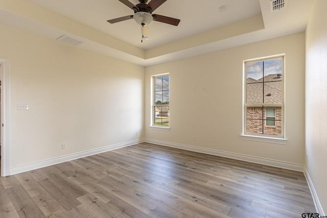 unfurnished room with ceiling fan, a tray ceiling, and light hardwood / wood-style flooring