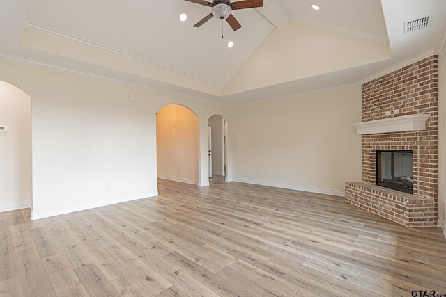 unfurnished living room with high vaulted ceiling, ceiling fan, crown molding, a brick fireplace, and light wood-type flooring