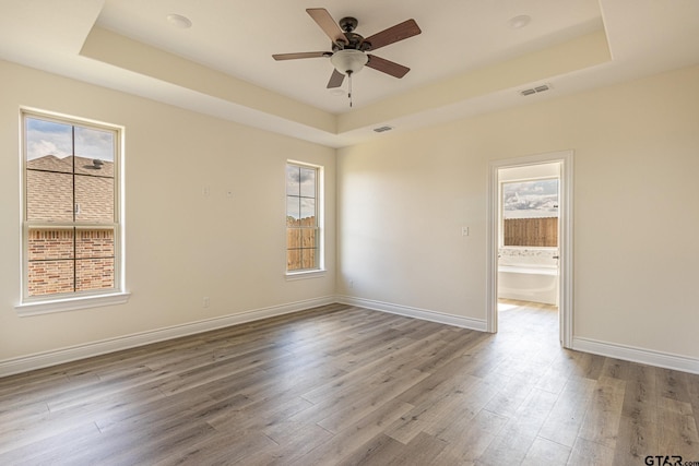 unfurnished room with a raised ceiling, wood-type flooring, and ceiling fan