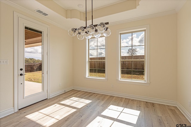 unfurnished dining area with a notable chandelier, ornamental molding, a raised ceiling, and light wood-type flooring