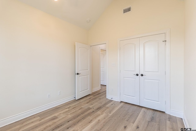 unfurnished bedroom featuring high vaulted ceiling, a closet, and light wood-type flooring