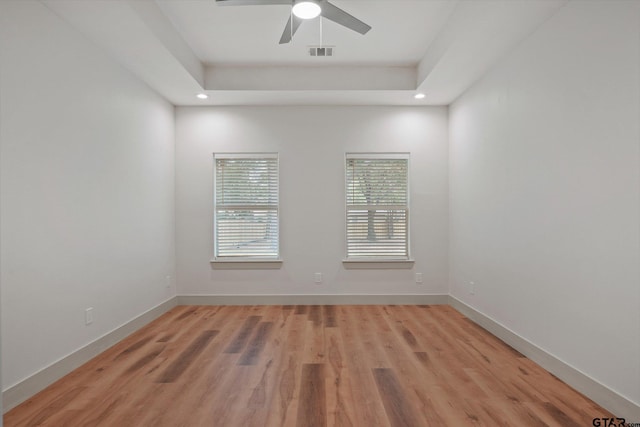 spare room featuring light hardwood / wood-style floors, ceiling fan, and a tray ceiling