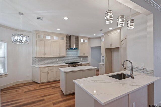 kitchen with wall chimney exhaust hood, decorative light fixtures, sink, and a center island