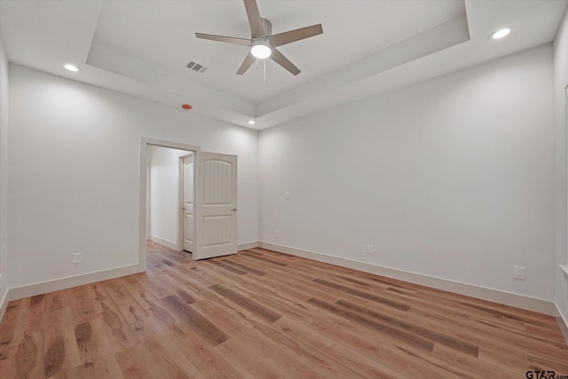 empty room with light wood-type flooring, ceiling fan, and a raised ceiling