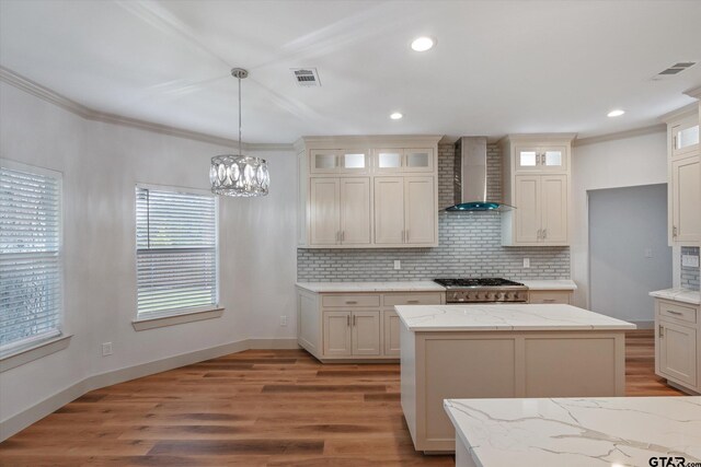 kitchen featuring light hardwood / wood-style floors, wall chimney range hood, a kitchen island, crown molding, and pendant lighting