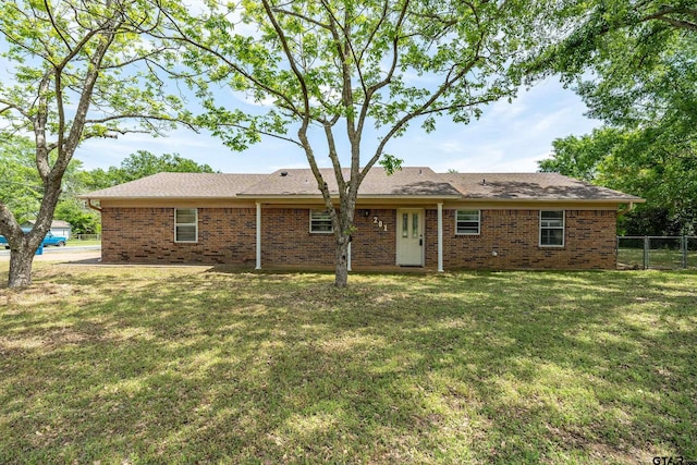 rear view of property featuring brick siding, fence, and a yard