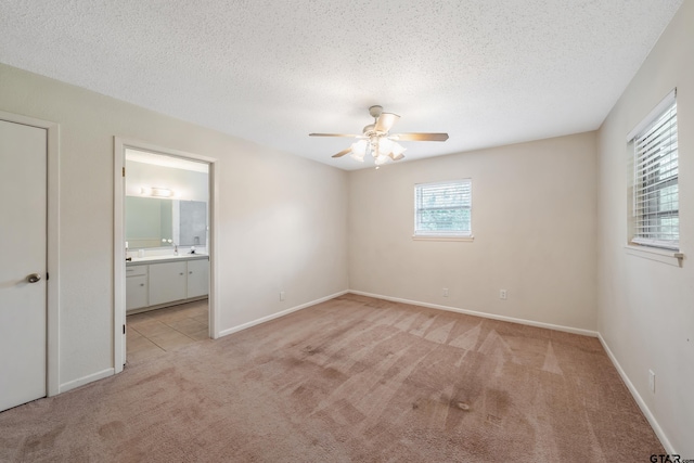unfurnished bedroom featuring connected bathroom, light colored carpet, a sink, baseboards, and a textured ceiling