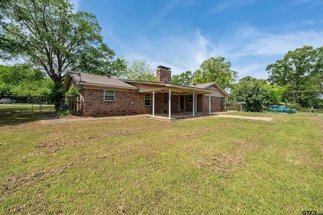back of property with a chimney, brick siding, a patio, and a yard
