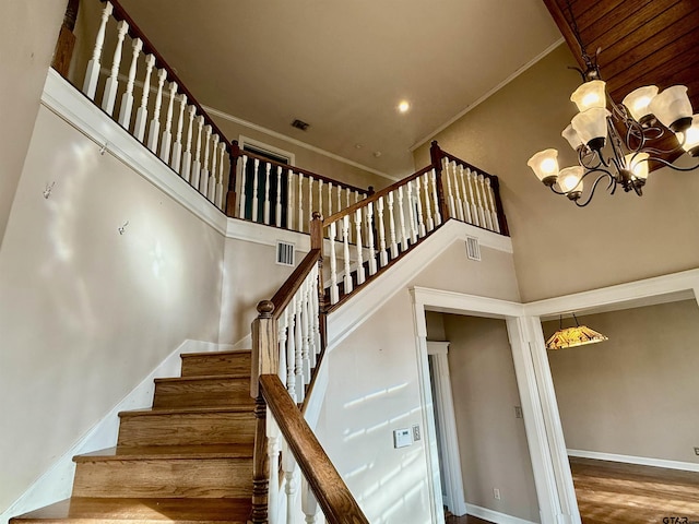 stairs featuring crown molding, a towering ceiling, a chandelier, and hardwood / wood-style flooring