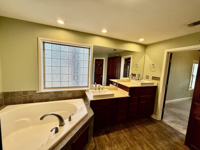 bathroom featuring hardwood / wood-style flooring, vanity, and tiled bath