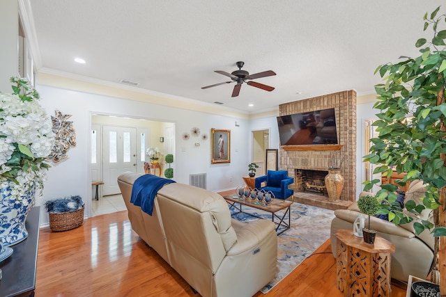 living area with ornamental molding, light wood-style floors, a brick fireplace, visible vents, and ceiling fan