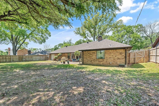 rear view of property featuring brick siding, a fenced backyard, a chimney, and a lawn