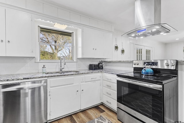 kitchen with appliances with stainless steel finishes, island exhaust hood, decorative backsplash, sink, and white cabinetry