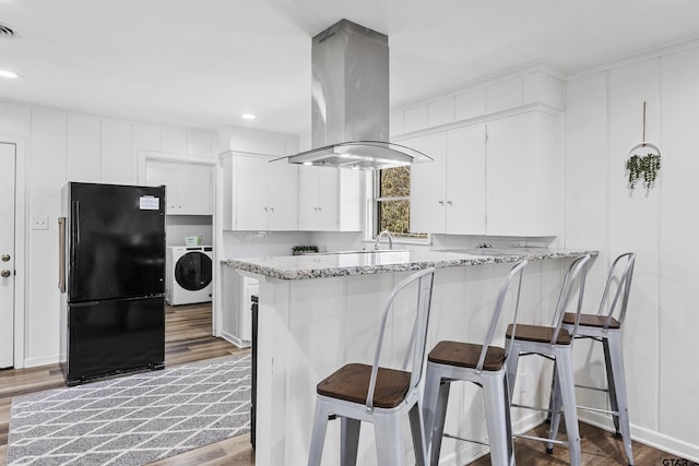 kitchen featuring kitchen peninsula, black refrigerator, light stone countertops, washer / clothes dryer, and island range hood