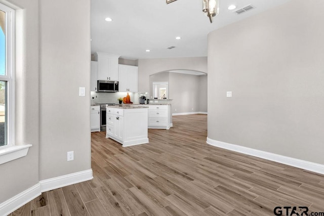 kitchen with visible vents, light wood finished floors, arched walkways, stainless steel appliances, and white cabinetry