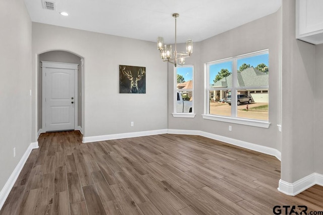 unfurnished dining area with visible vents, baseboards, wood finished floors, arched walkways, and a notable chandelier