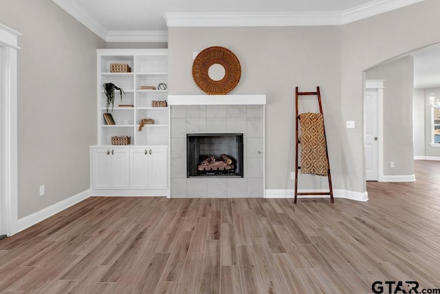 unfurnished living room with a tiled fireplace, wood finished floors, baseboards, and ornamental molding