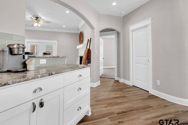 kitchen with light stone counters, baseboards, light wood finished floors, arched walkways, and white cabinetry