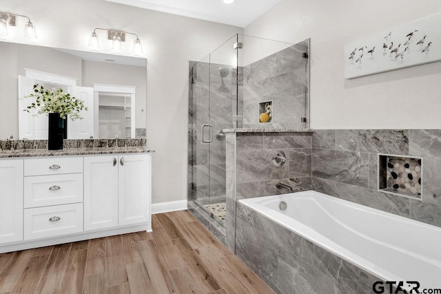 full bathroom with double vanity, a stall shower, wood finished floors, a bath, and a sink