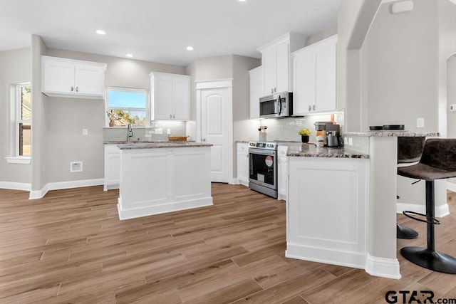 kitchen with a breakfast bar, white cabinetry, arched walkways, appliances with stainless steel finishes, and light wood finished floors