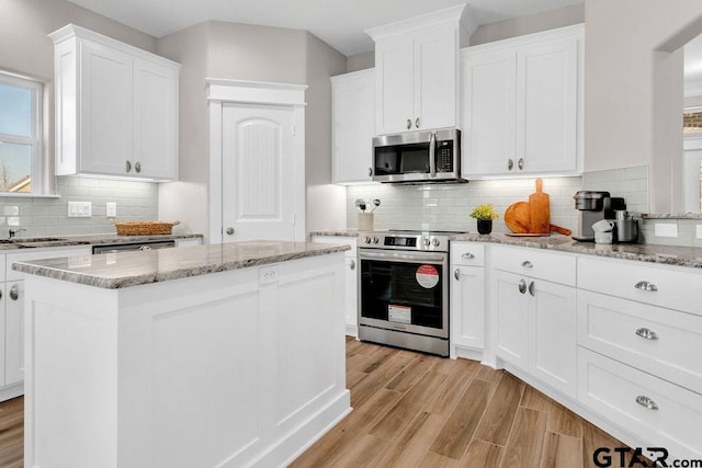 kitchen with light wood-type flooring, white cabinets, appliances with stainless steel finishes, tasteful backsplash, and a center island