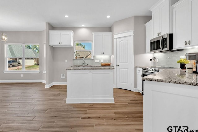 kitchen with baseboards, decorative backsplash, light wood-style floors, white cabinetry, and stainless steel microwave