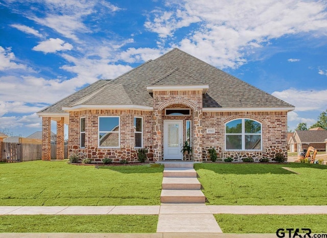 french country home with a front lawn, fence, brick siding, and a shingled roof