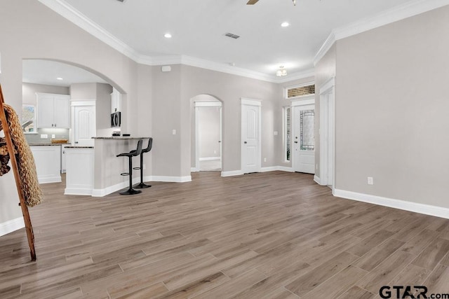 unfurnished living room with visible vents, ornamental molding, arched walkways, light wood finished floors, and ceiling fan