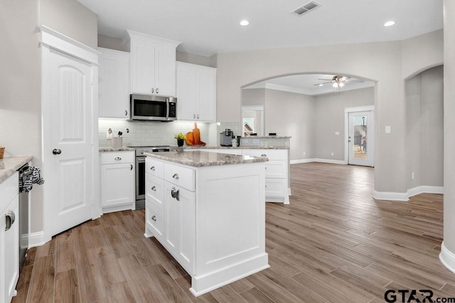 kitchen with visible vents, light wood finished floors, arched walkways, decorative backsplash, and appliances with stainless steel finishes