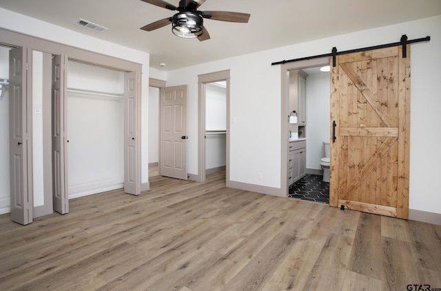 unfurnished bedroom featuring a barn door, connected bathroom, and light wood-type flooring