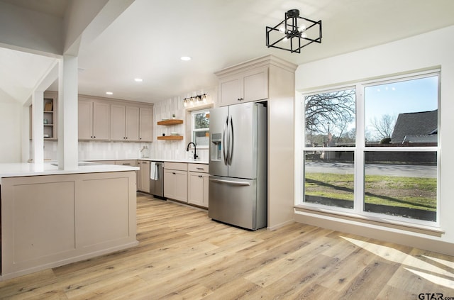 kitchen with hanging light fixtures, light wood-type flooring, kitchen peninsula, stainless steel appliances, and backsplash