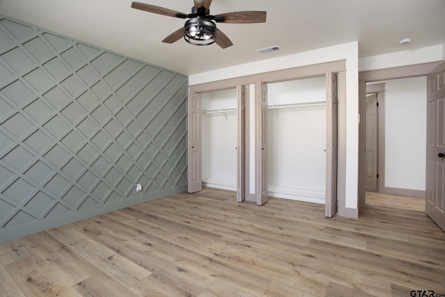 unfurnished bedroom featuring ceiling fan, light wood-type flooring, and two closets