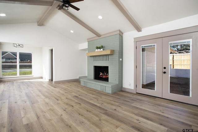 unfurnished living room featuring a brick fireplace, a healthy amount of sunlight, beam ceiling, and french doors