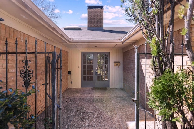 entrance to property with brick siding, a patio area, french doors, and a chimney