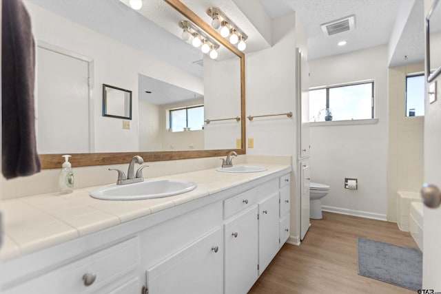 bathroom with toilet, wood finished floors, visible vents, and a sink