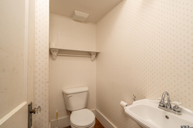 bathroom with visible vents, baseboards, wallpapered walls, toilet, and a sink