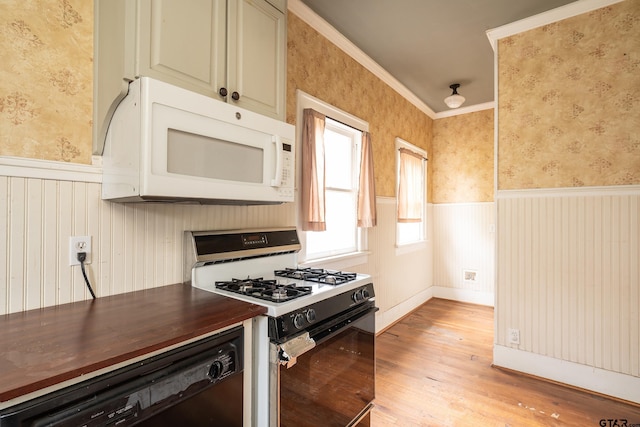 kitchen featuring white microwave, wallpapered walls, range with gas cooktop, and wainscoting