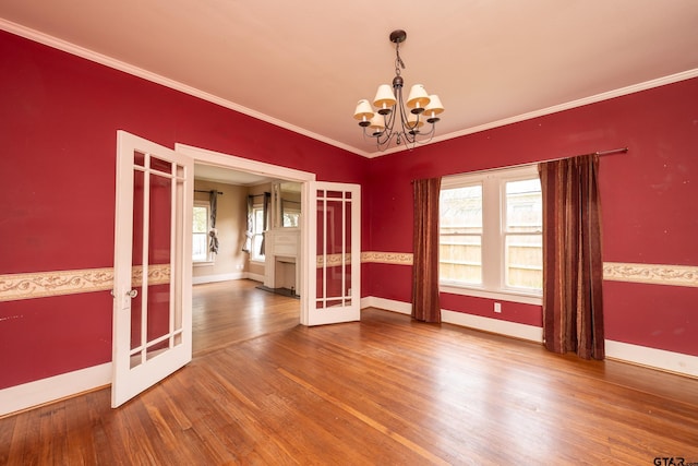 spare room featuring an inviting chandelier, crown molding, a healthy amount of sunlight, and wood finished floors
