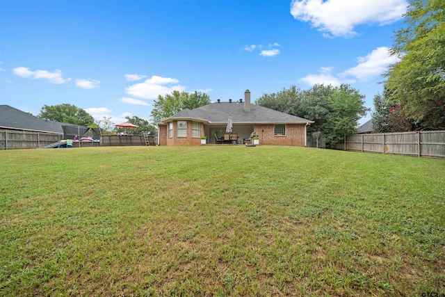 back of house with a yard, a fenced backyard, brick siding, and a chimney