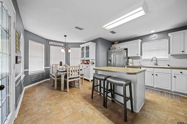 kitchen with stainless steel fridge, white cabinetry, a breakfast bar area, and a sink