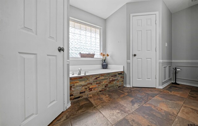 full bathroom with stone tile flooring and a bath